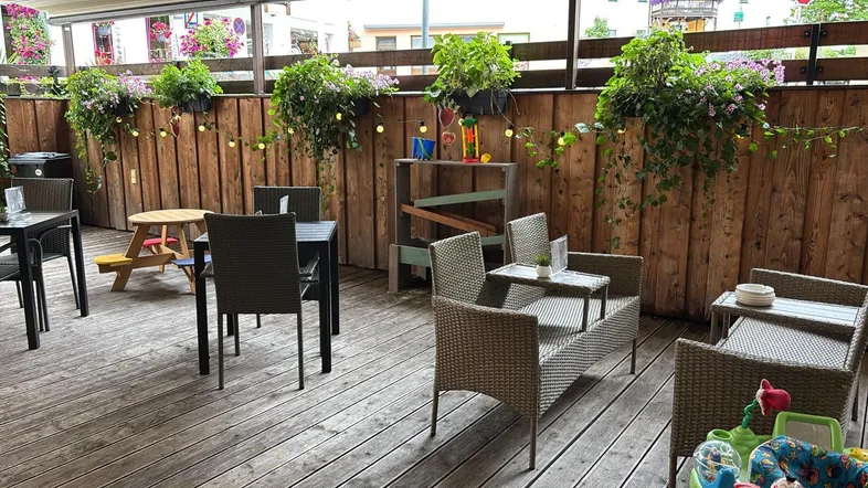 Gemütliche Außenterrasse mit Holzboden, Flechtmöbeln und üppiger Bepflanzung, ideal zum Entspannen im Freien.