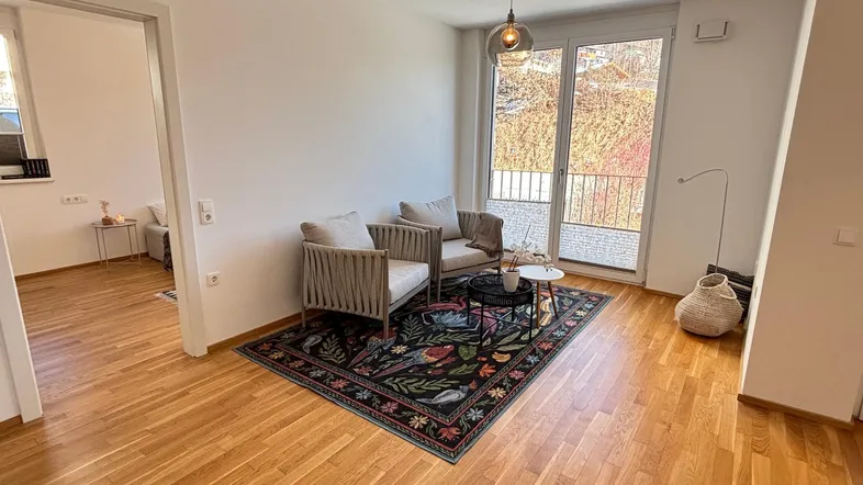 Helles Wohnzimmer mit Holzboden, gemütlichen Sesseln und Zugang zu einem Balkon mit Ausblick.