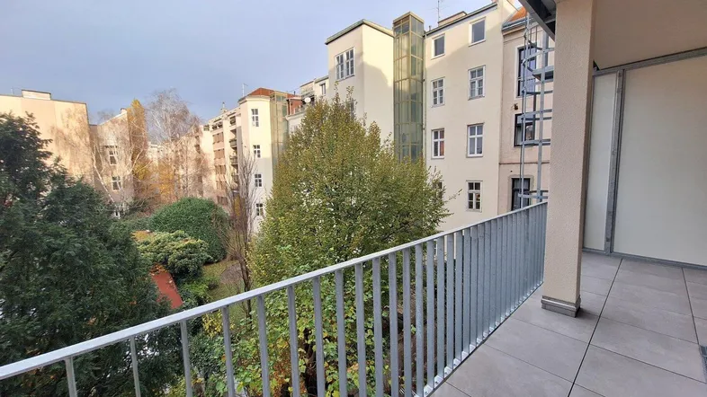 Geräumiger Balkon mit Blick auf den begrünten Innenhof und umliegende Gebäude.