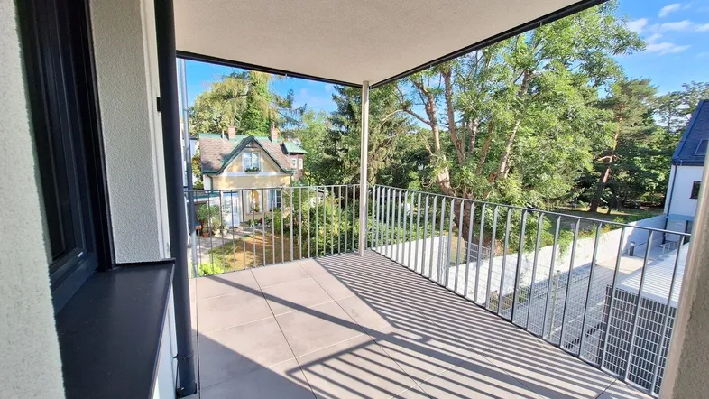 Heller Balkon mit Fliesenboden und Metallgeländer, bietet einen schönen Blick ins Grüne.