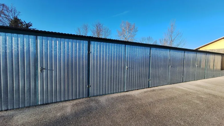 Reihe von gut erhaltenen Lagerboxen oder Garagen mit Wellblechfassade unter klarem blauem Himmel.