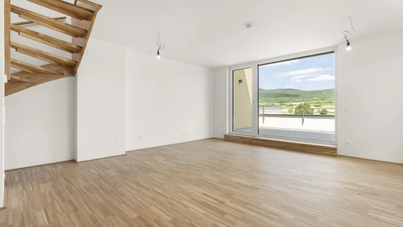 Helles Wohnzimmer mit Holztreppe, Parkettboden und weitem Blick ins Grüne.