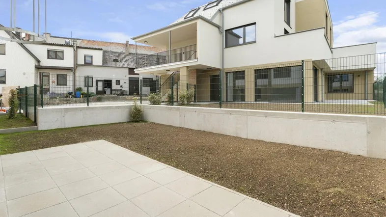 Moderne Wohnanlage mit weißer Fassade, großzügigen Fenstern und einem noch ungestalteten Gartenbereich.