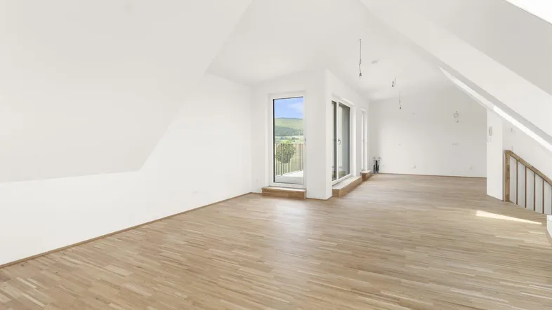 Helles Zimmer im Dachgeschoss mit Holzboden und Zugang zu einem Balkon mit Weitblick.