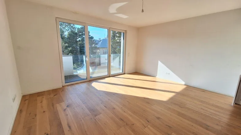 Helles Zimmer mit Holzboden und großen Schiebetüren, die auf einen Balkon führen.