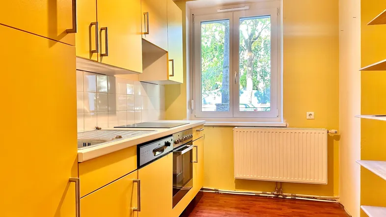 Gelbe Einbauküche mit Induktionskochfeld, Backofen und Fenster mit Blick ins Grüne.