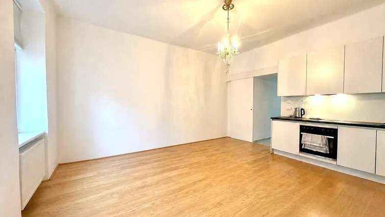 Helles Zimmer mit Holzboden, Kronleuchter und integrierter Küchenzeile, ideal für offenes Wohnen.