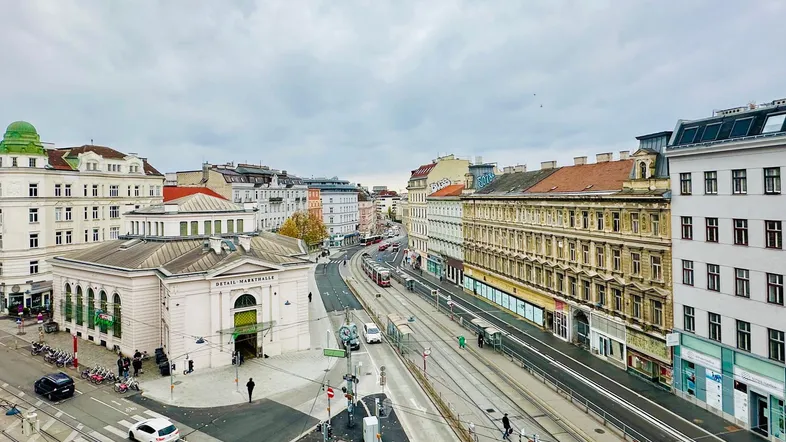 Weitläufiger Blick über eine belebte Stadtstraße mit Straßenbahnen und historischen Gebäuden.