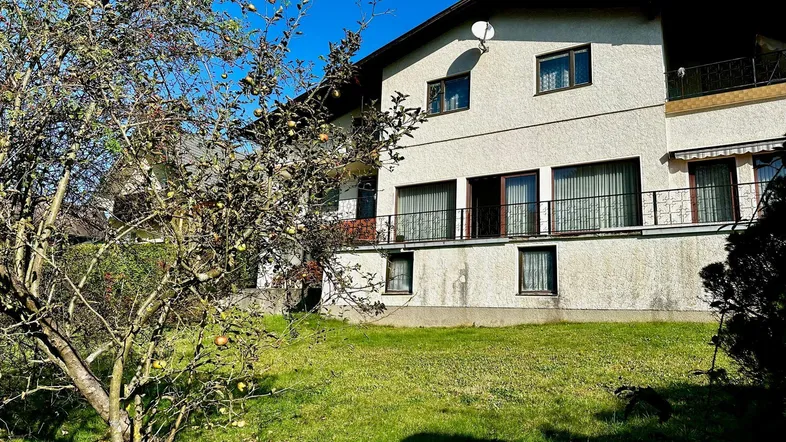 Fassade eines Wohnhauses mit Balkonen und einem Obstbaum im Vordergrund an einem sonnigen Tag.