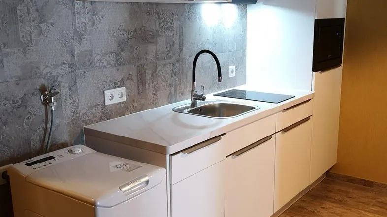 Kleine, moderne Küche mit weißen Schränken, Induktionskochfeld, Mikrowelle und integrierter Waschmaschine.