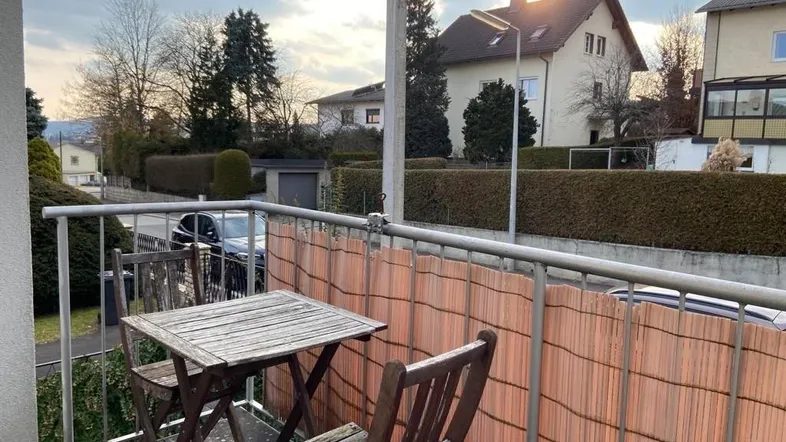 Kleiner Balkon mit Holztisch und Stühlen, bietet einen Blick auf die Straße und umliegende Häuser.