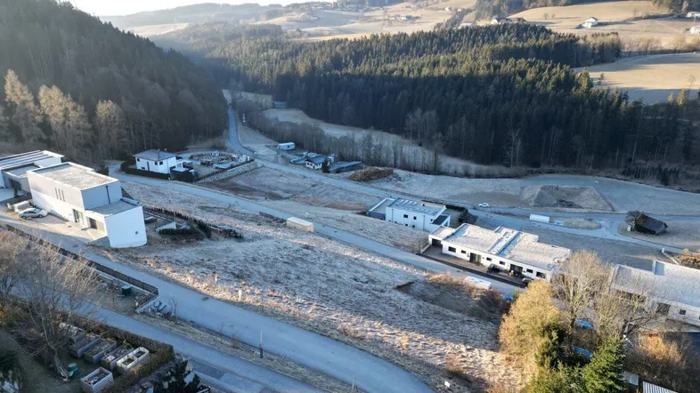 Luftaufnahme eines Tals mit verstreuten Häusern, Straßen und bewaldeten Hügeln unter klarem Himmel.