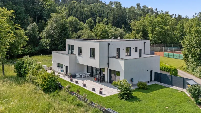 Moderne Villa mit großer Terrasse, umgeben von Wald und mit eigenem Tennisplatz.