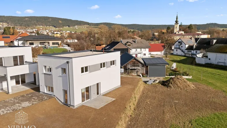 Moderne Neubau-Doppelhaushälfte mit Flachdach und Blick auf die ländliche Umgebung und Kirchturm.