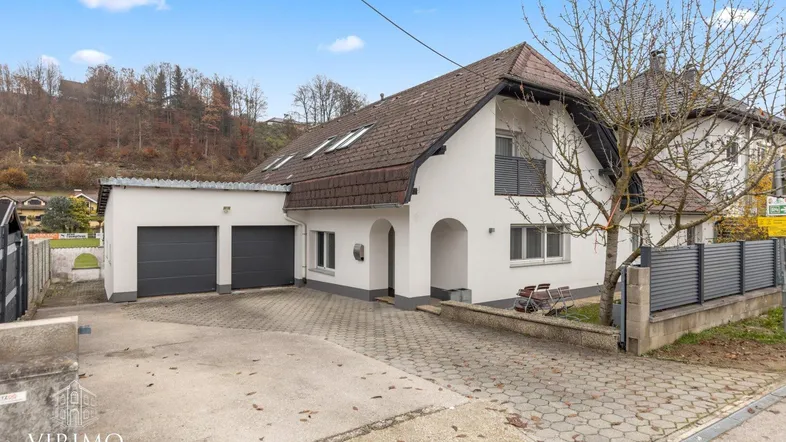 Weißes Einfamilienhaus mit Satteldach, Doppelgarage und gepflasterter Auffahrt.