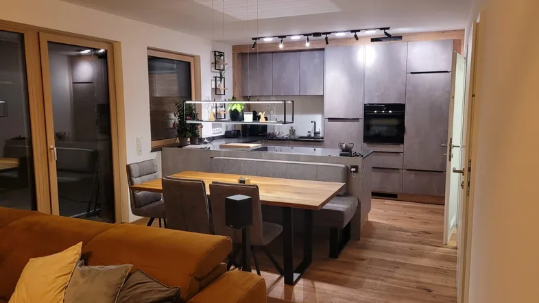 Moderne offene Küche mit grauen Schränken, Holzboden und integriertem Essbereich, verbunden mit dem Wohnzimmer.