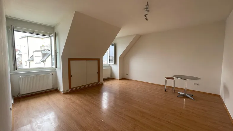 Helles Dachgeschosszimmer mit Holzboden, schrägen Wänden und zwei Fenstern, ideal als Wohn- oder Schlafzimmer.