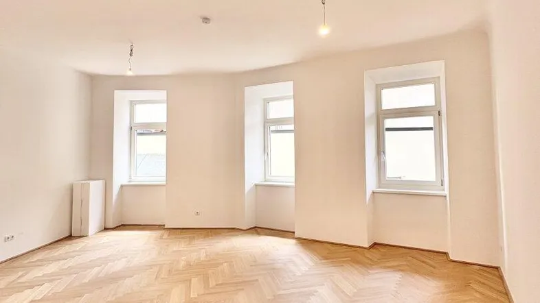 Helles, leeres Zimmer mit Fischgrätparkett und mehreren Fenstern, bereit zur Einrichtung.
