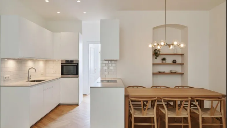 Helle, moderne Wohnküche mit weißer Einbauküche, Holzboden und Essbereich für mehrere Personen.
