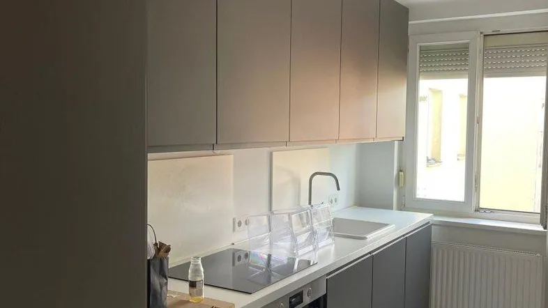 Moderne Küche mit grauen Hochglanzschränken, Induktionskochfeld und Backofen, sowie einem Fenster.