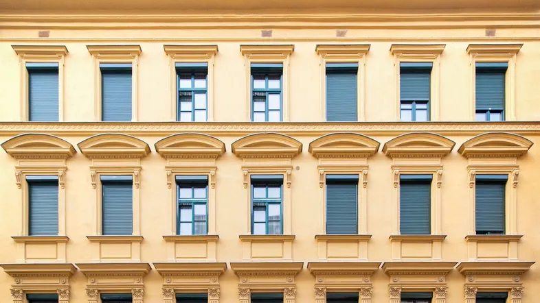 Gelbe historische Fassade eines Gebäudes mit vielen Fenstern und einem roten Roller davor.