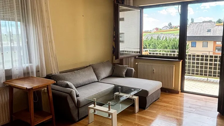 Helles Wohnzimmer mit Parkettboden, gemütlichem Sofa und Zugang zu einem Balkon mit Weitblick.
