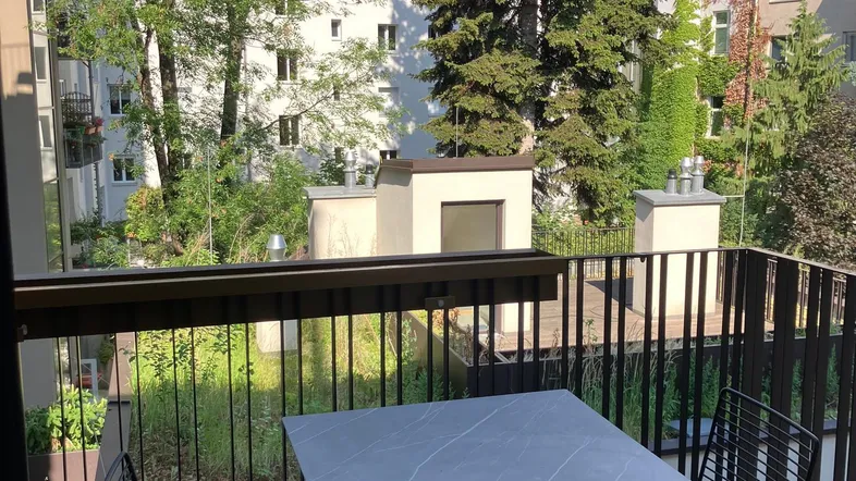 Möblierter Balkon mit Tisch und Stühlen, bietet einen grünen Blick auf Bäume und umliegende Gebäude.