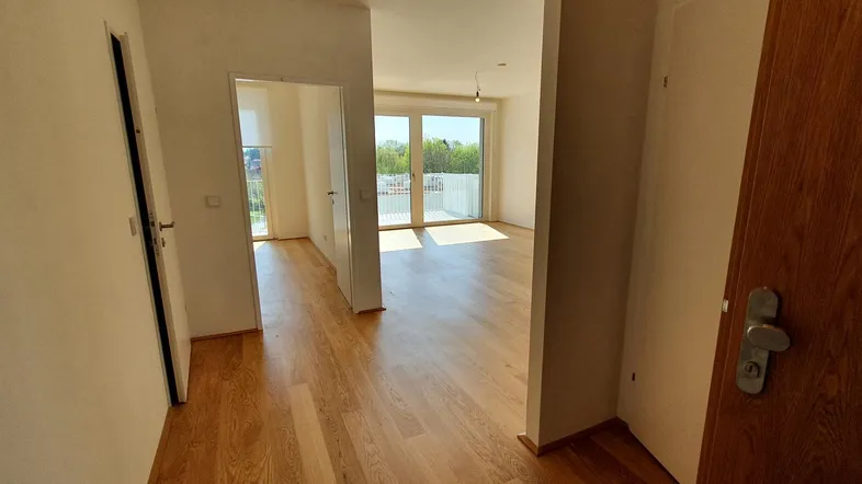 Heller Eingangsbereich mit Holzfußboden, der in einen lichtdurchfluteten Wohnbereich mit Balkonzugang führt.