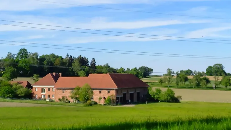 Ländliches Anwesen mit mehreren Gebäuden, umgeben von grünen Feldern unter blauem Himmel.