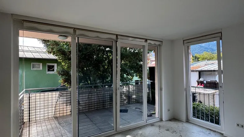 Helles Wohnzimmer mit großflächigen Fenstern, Zugang zum Balkon und Blick auf die Berge.