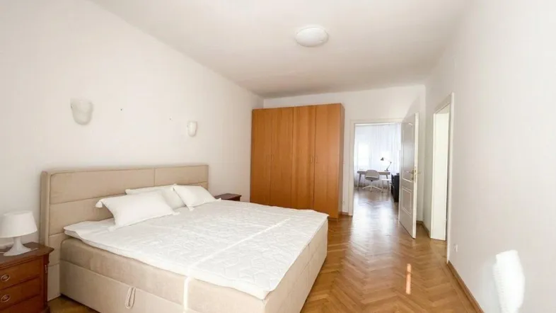 Helles Schlafzimmer mit Fischgrätparkett, weiß gestrichenen Wänden und einem großen Kleiderschrank.
