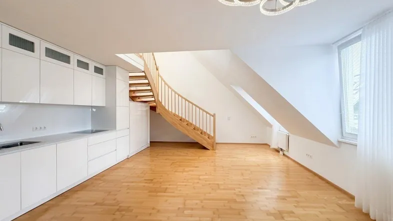 Heller offener Wohnbereich mit moderner Küchenzeile, Holztreppe und Dachschrägenfenster.