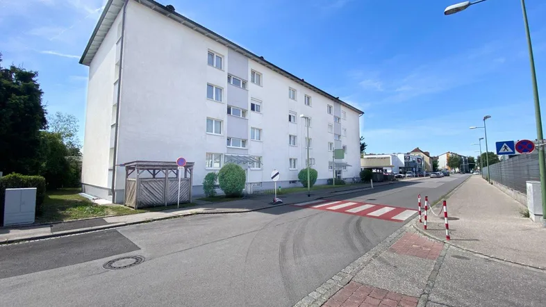 Mehrfamilienhaus mit weißer Fassade und gepflegter Umgebung an einer ruhigen Straße.