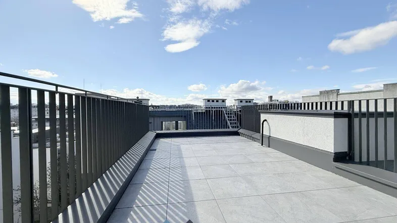 Große, geflieste Dachterrasse mit Metallgeländer und weitem Blick über die Stadt.
