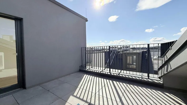 Geräumige Dachterrasse mit Fliesenboden und Blick auf die Umgebung unter strahlendem Sonnenschein.