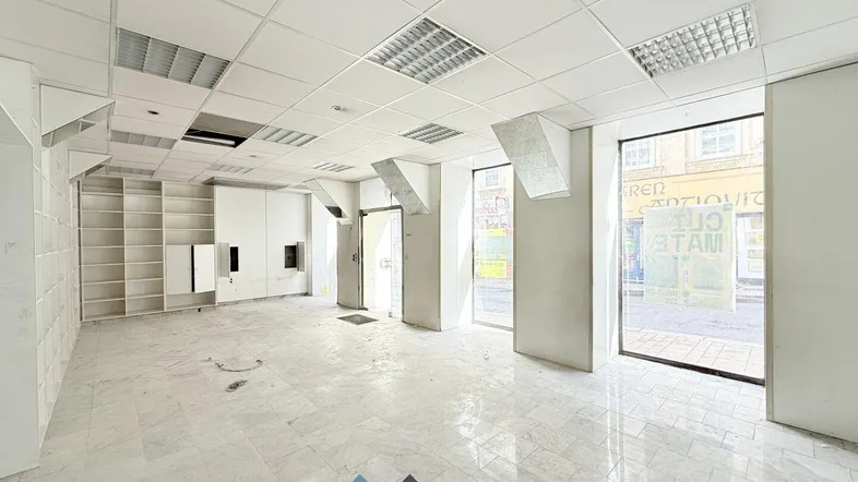 Heller Verkaufsraum mit großen Schaufenstern, Fliesenboden und abgehängter Decke, bereit zur Renovierung.