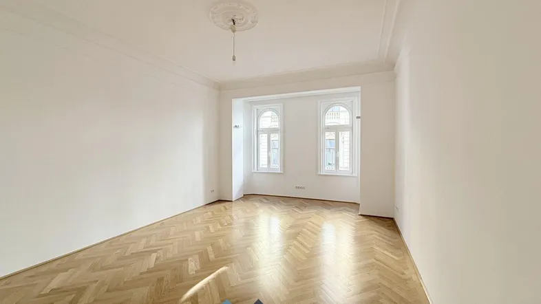 Helles Wohnzimmer mit Fischgrätparkett, hohen Decken und dekorativer Stuckverzierung an der Decke.