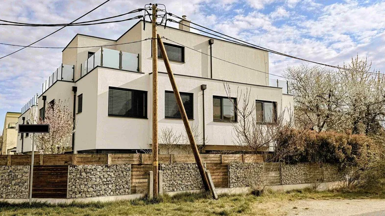 Modernes Mehrfamilienhaus mit weißer Fassade und großen Fenstern unter bewölktem Himmel.