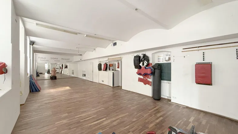 Großer Trainingsraum mit Holzboden, Spiegelwand und Boxsäcken, ideal für Kampfsport oder Fitness.