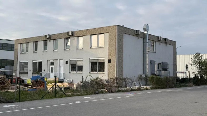 Gebäudeansicht eines zweistöckigen Gewerbebaus mit mehreren Fenstern und Klimaanlagen an der Fassade.