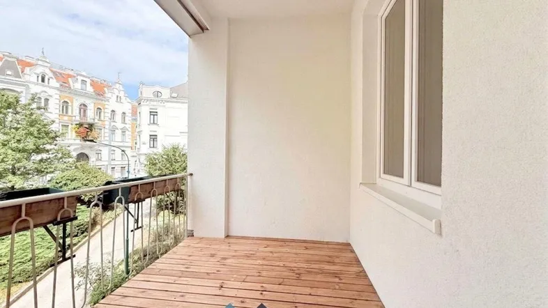 Heller Balkon mit Holzboden und Blick auf die umliegenden Gebäude und Bäume.