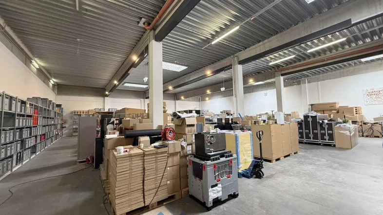 Großer Lagerraum mit hohen Decken, Oberlichtern und zahlreichen Kartons sowie Regalen für die Lagerung von Waren.