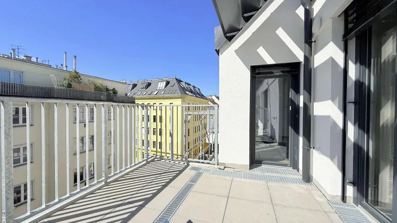 Geräumiger Balkon mit Metallgeländer und Blick auf die umliegenden Gebäude unter blauem Himmel.