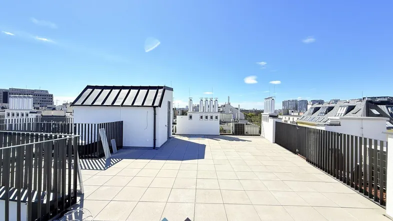 Große Dachterrasse mit Fliesenboden und Blick auf die Stadt unter blauem Himmel.