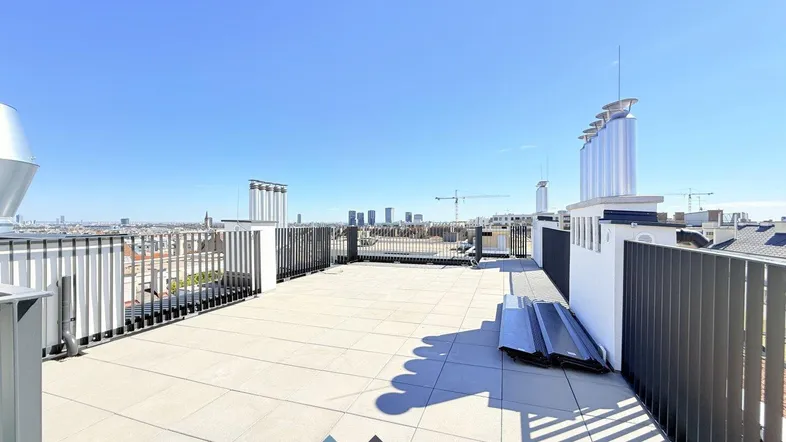 Große Dachterrasse mit weitem Blick über die Stadt und moderne Architektur im Hintergrund.