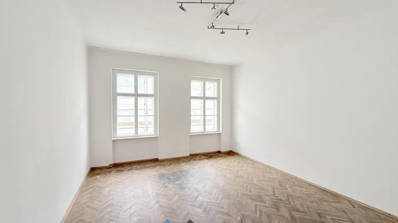 Helles, leeres Zimmer mit Fischgrätparkett und zwei Fenstern, bereit zur individuellen Gestaltung.
