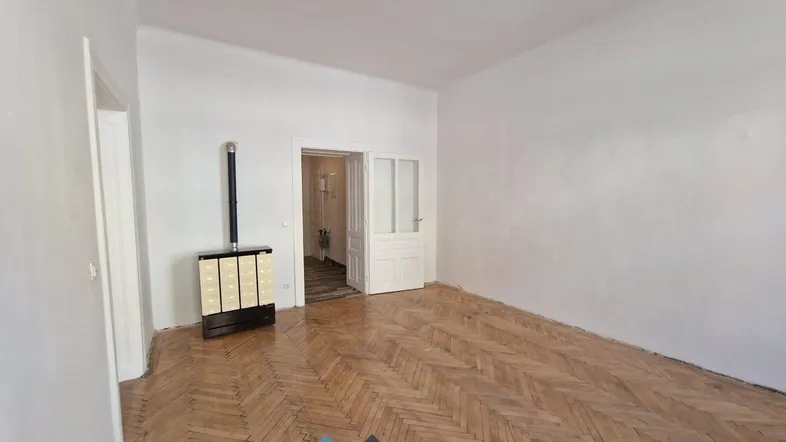 Geräumiges Zimmer mit Fischgrätparkett und einem traditionellen Ofen, bereit zur individuellen Gestaltung.