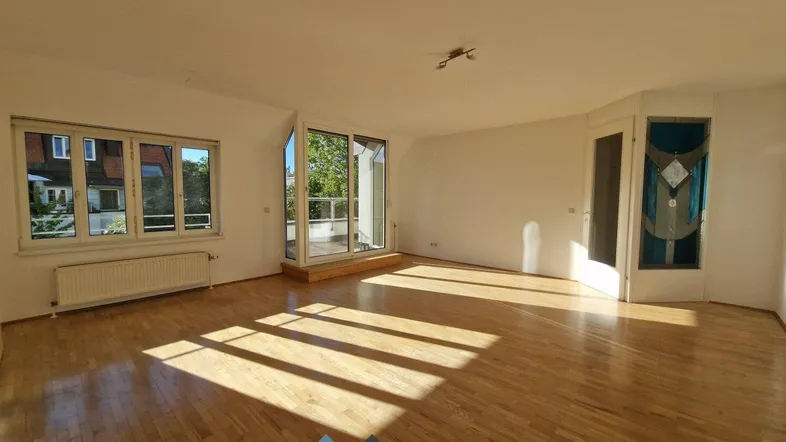Helles Wohnzimmer mit Parkettboden, großen Fenstern und Zugang zu einem Balkon.