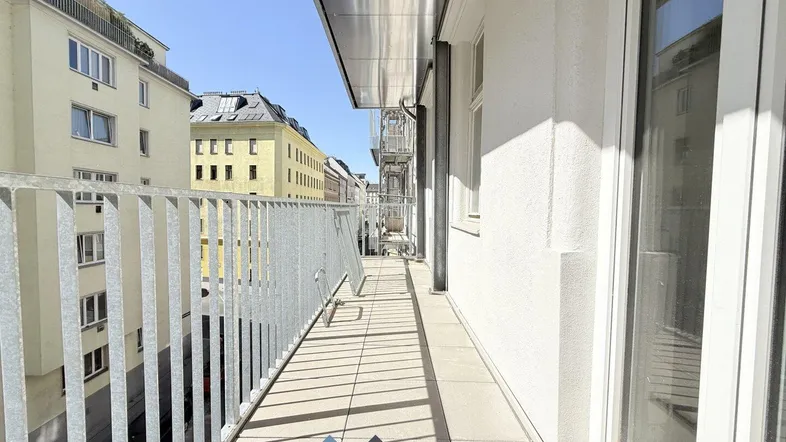 Langer, sonniger Balkon mit Metallgeländer und Blick auf die umliegenden Gebäude der Stadt.