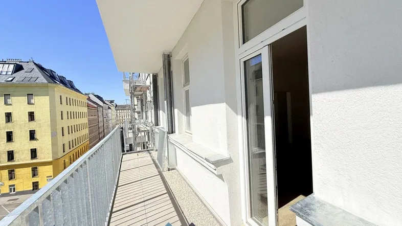 Langer, schmaler Balkon mit Blick auf die umliegenden Stadtgebäude und viel Tageslicht.